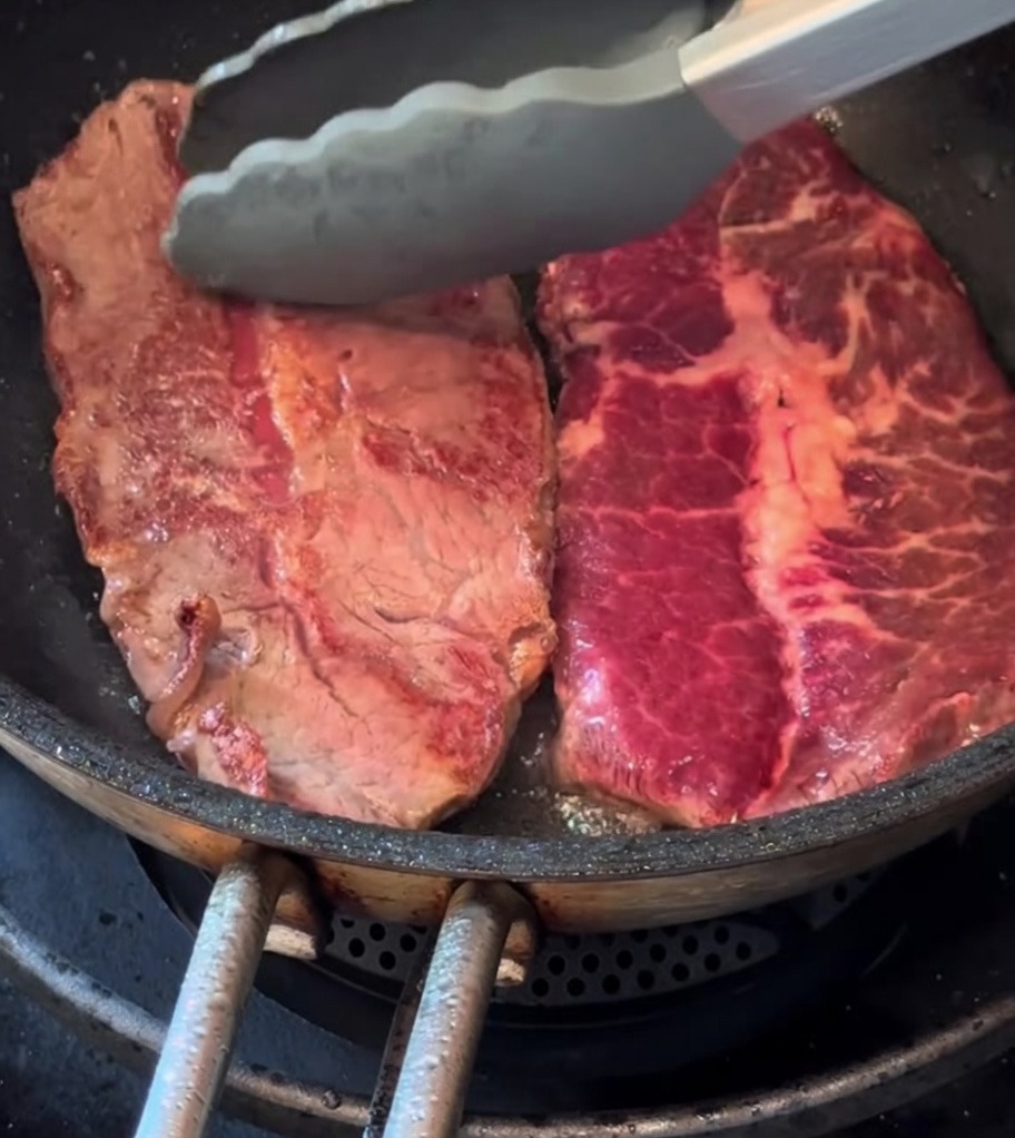 Deux steaks fins dorent dans une poêle avec une branche de romarin frais.