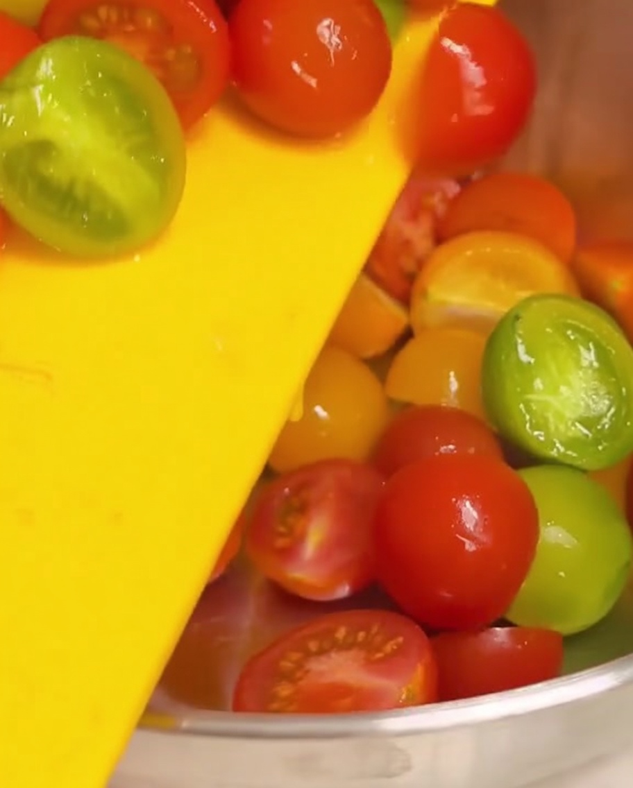 Des demi-tomates cerises poussées dune planche à découper jaune dans un bol mélangeur en acier inoxydable.