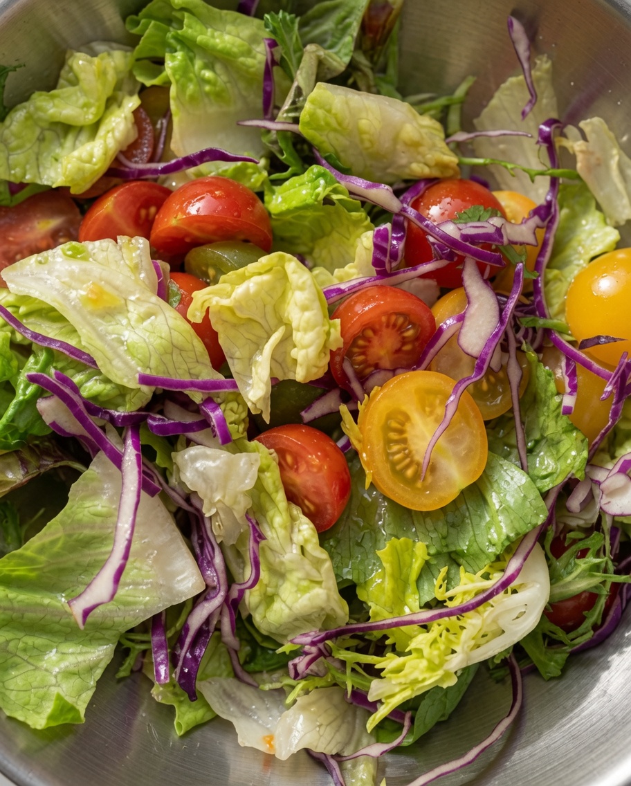 Une salade mixte vibrante de laitue verte, de chou rouge et de tomates cerises coupées en deux, mélangées ensemble dans un bol en métal.