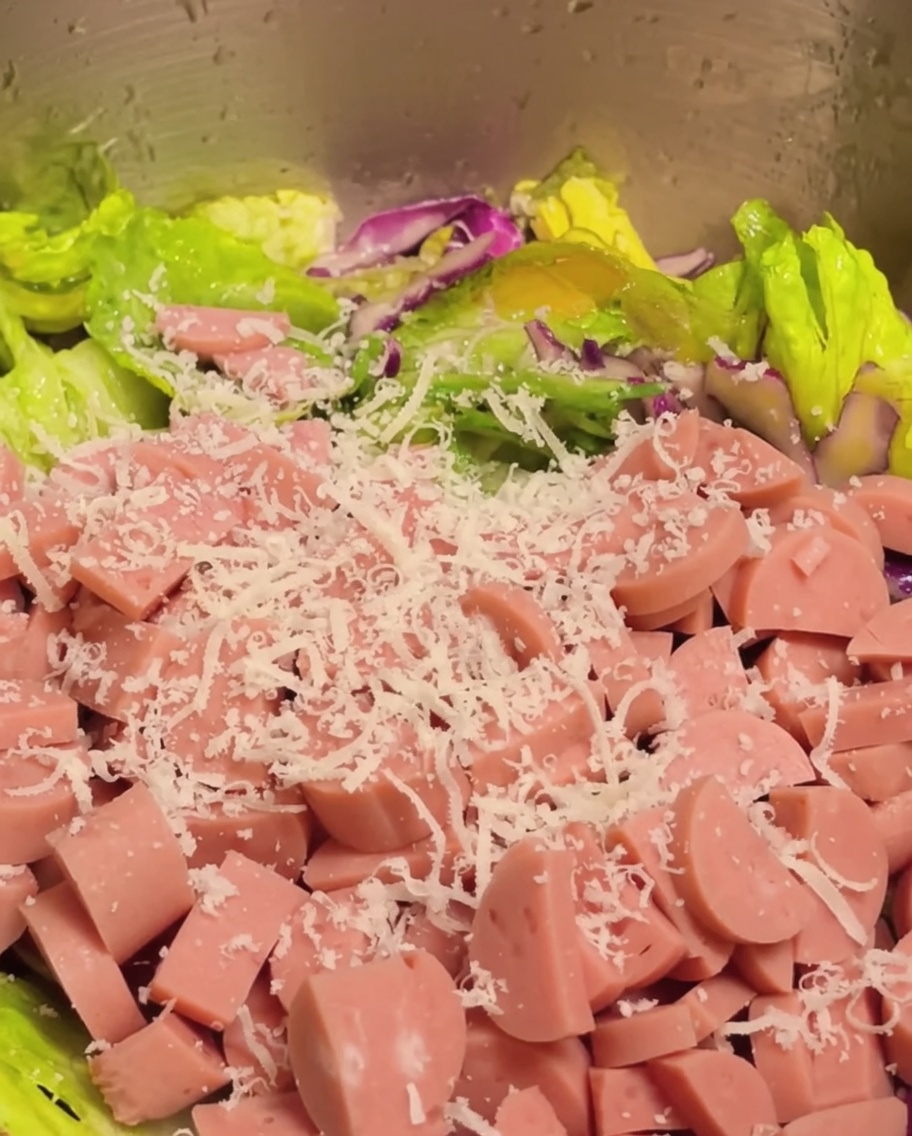 Jambon coupé en dés et parmesan râpé ajoutés au mélange de légumes de la salade.