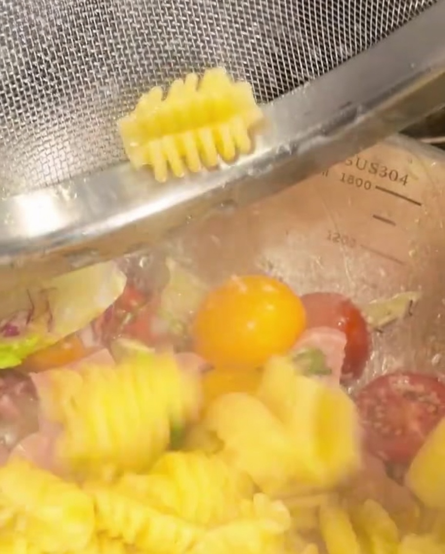 Des pâtes spirales cuites transférées dans un bol avec des légumes et du jambon.