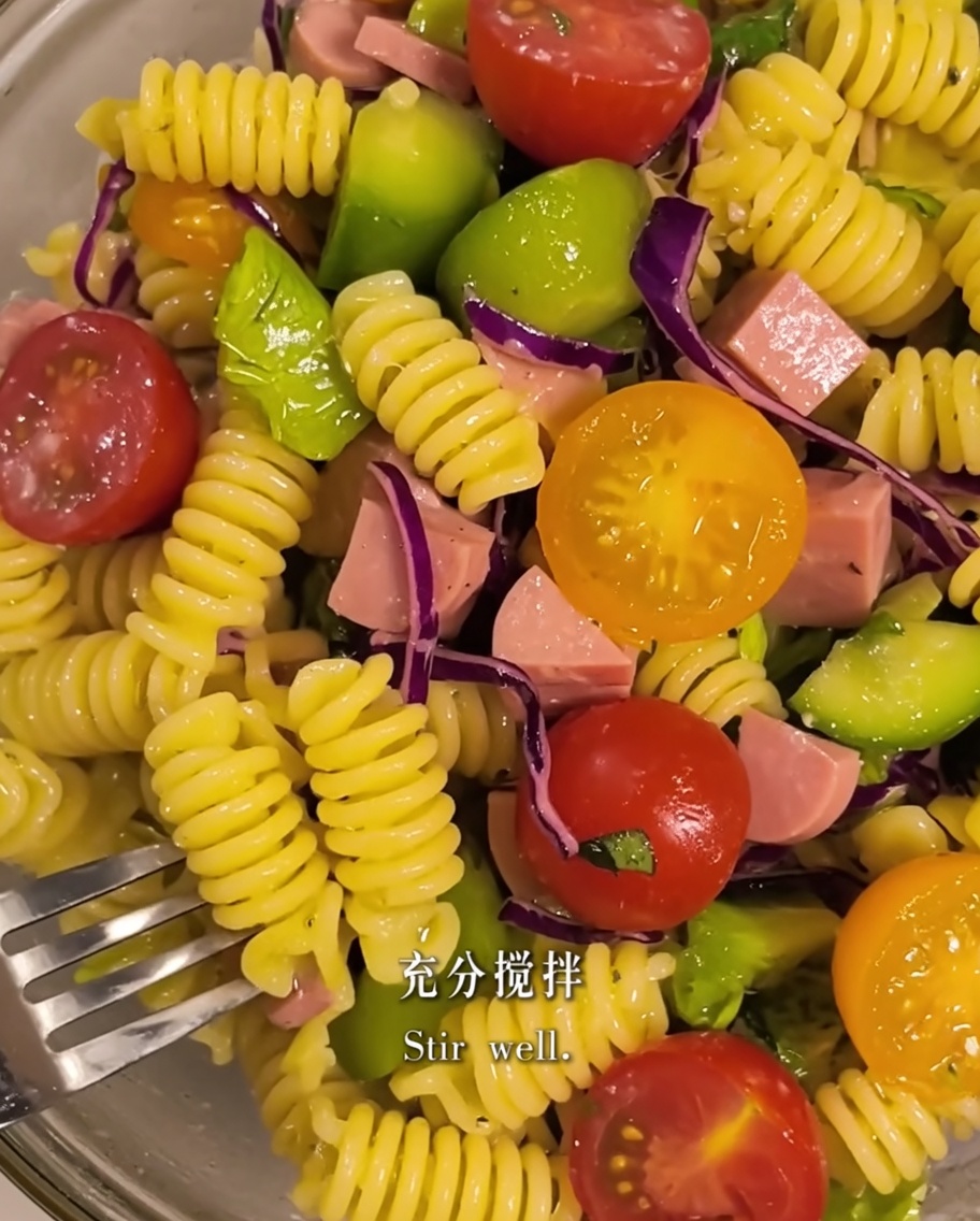 Pâtes et ingrédients de la salade mélangés avec de lhuile dolive dans un bol.