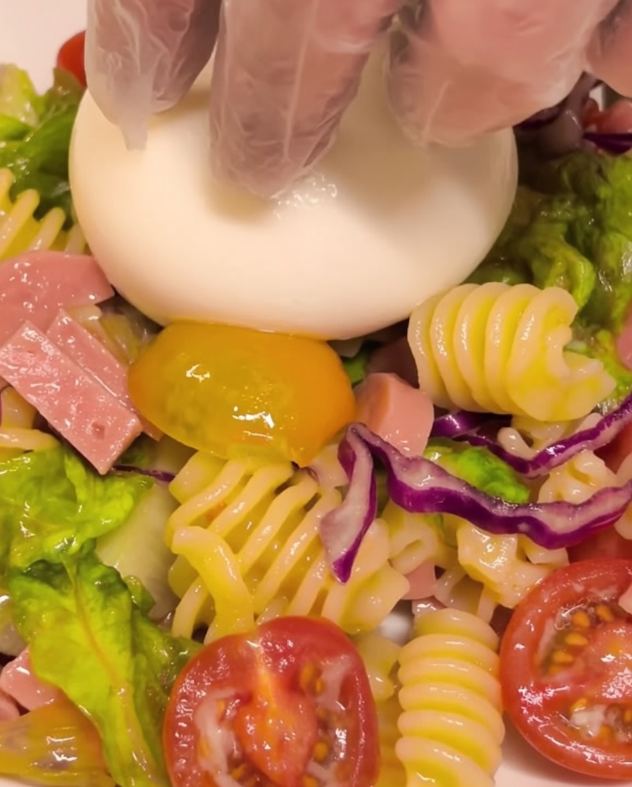 Une boule de burrata fraîche placée au centre dune portion de salade de pâtes froides.