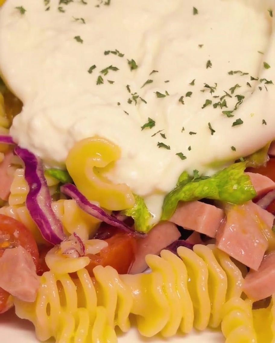 Gros plan de la burrata crémeuse, coupée en deux, assaisonnée de persil vert finement haché et de flocons de piment rouge.