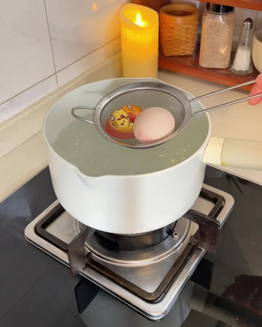Des œufs plongés délicatement dans une casserole deau bouillante à laide dune passoire en acier inoxydable.