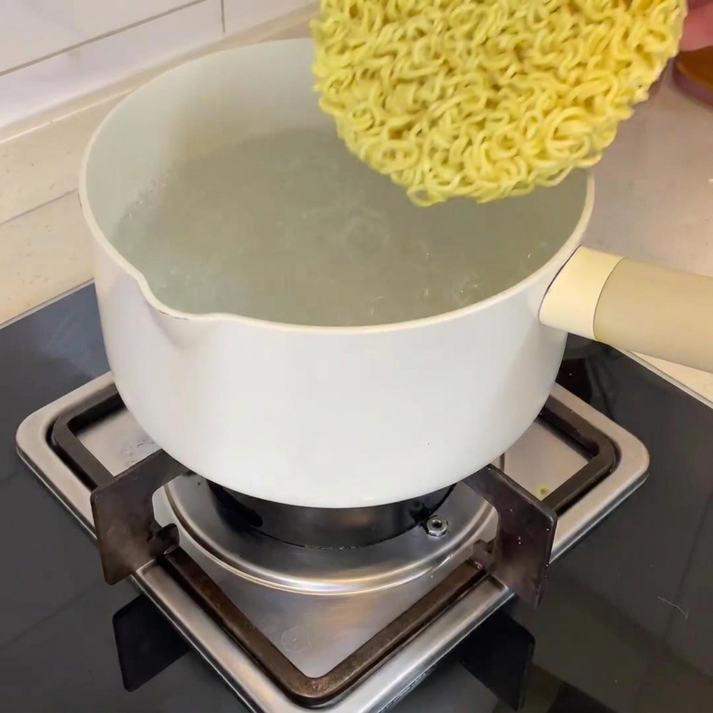 Un bloc de nouilles ramen séchées plongé dans une casserole deau bouillante.
