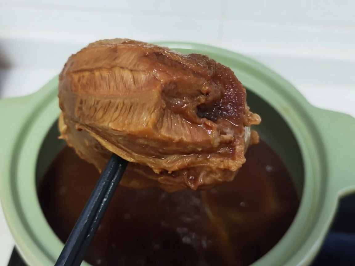 Un jarret de bœuf cuit et bruni en train dêtre enveloppé serré dans du film alimentaire transparent.