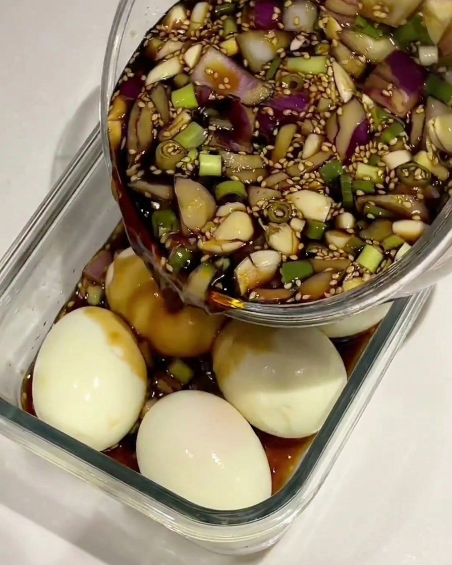 La marinade à la sauce soja versée sur des œufs durs écalés dans un récipient en verre.