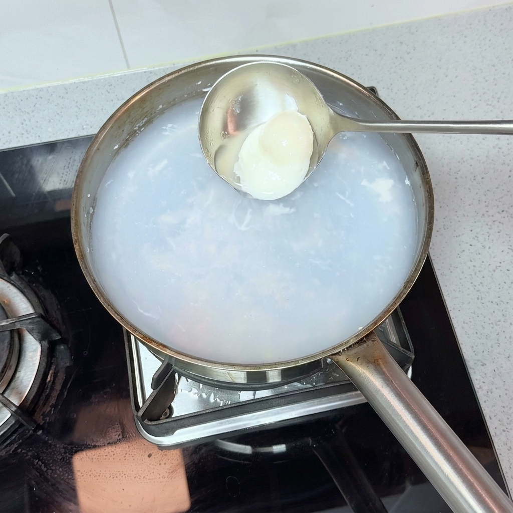 Une louche en métal repêchant délicatement un œuf parfaitement poché dans une casserole deau chaude.