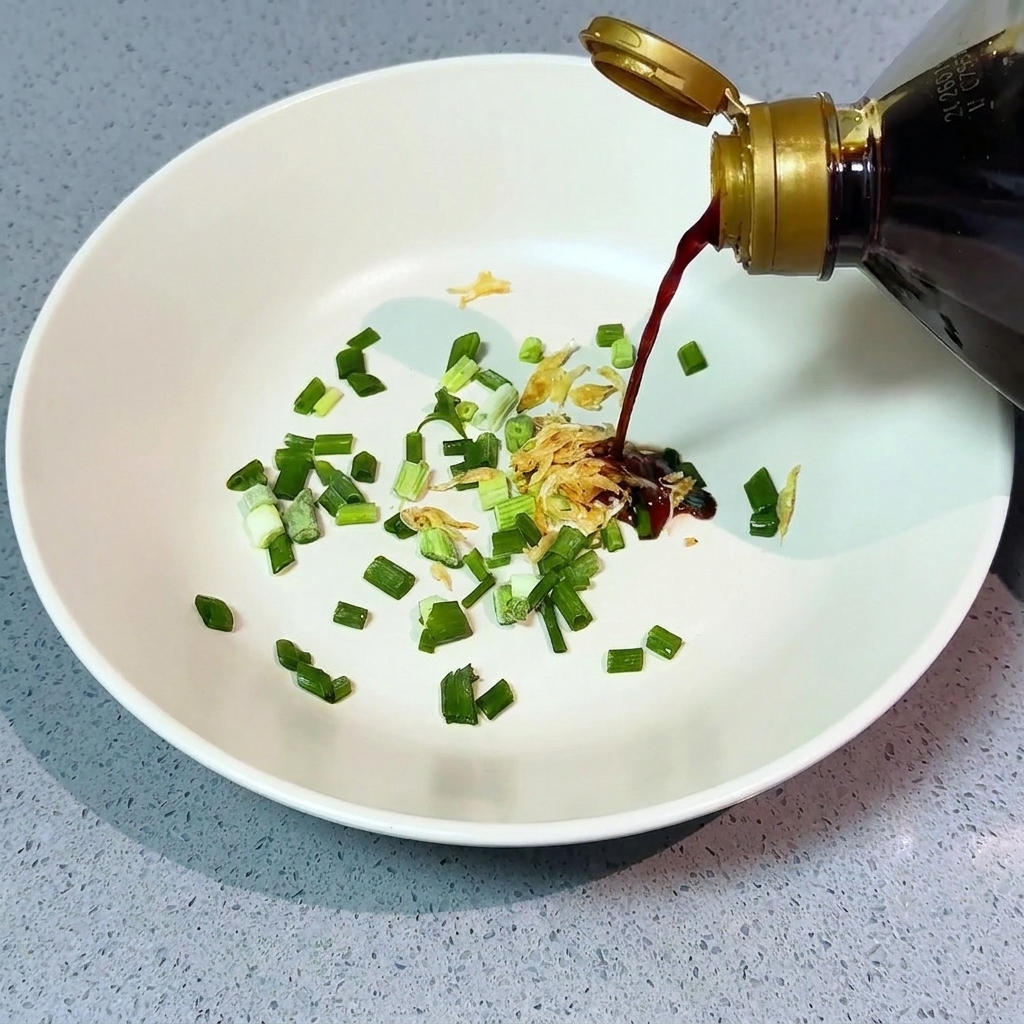 Verser de la sauce soja claire depuis une bouteille sur la cébette hachée et les crevettes séchées dans un bol blanc.