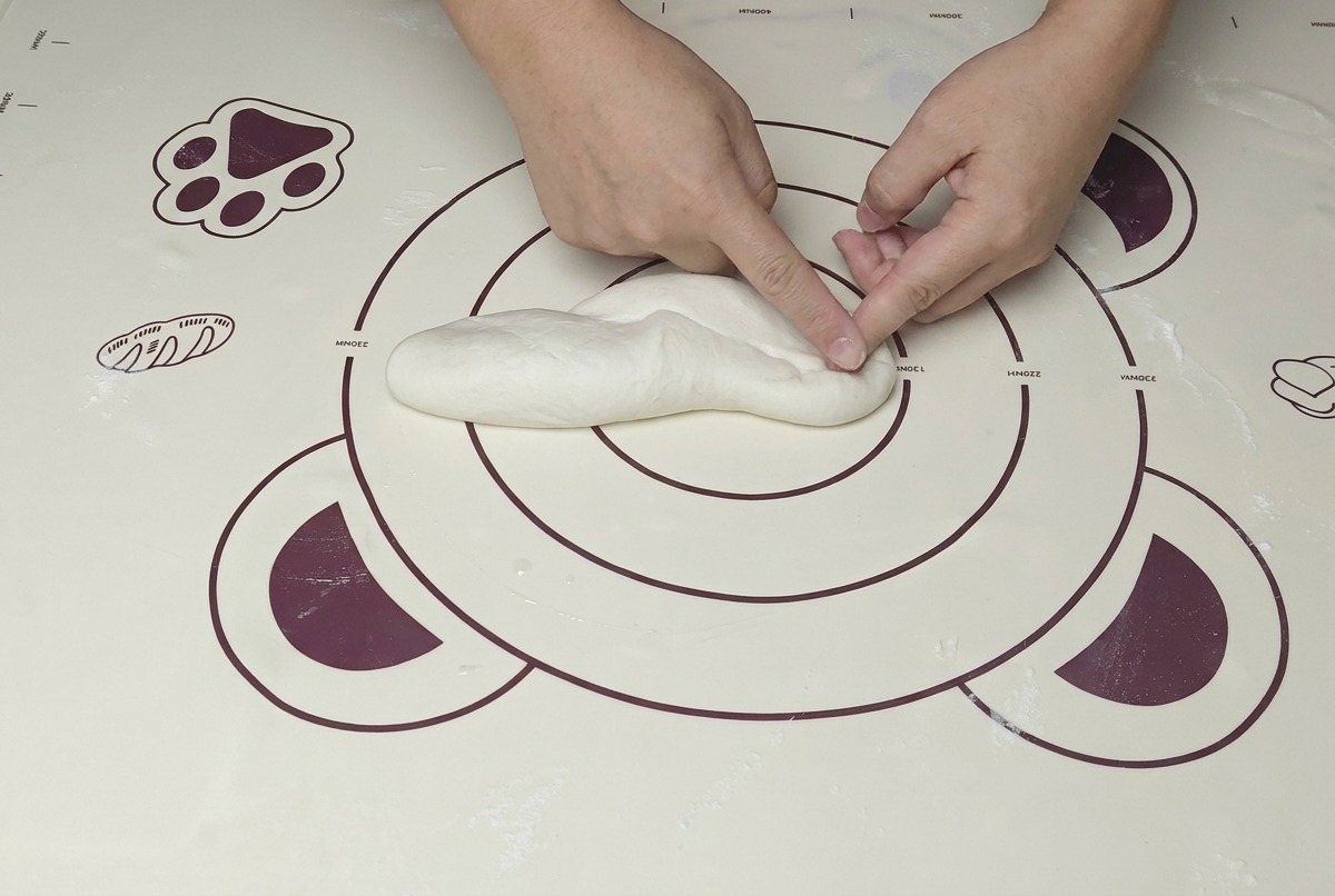 Une paire de mains pétrissant une boule de pâte sur un tapis, utilisant la paume pour presser fermement.