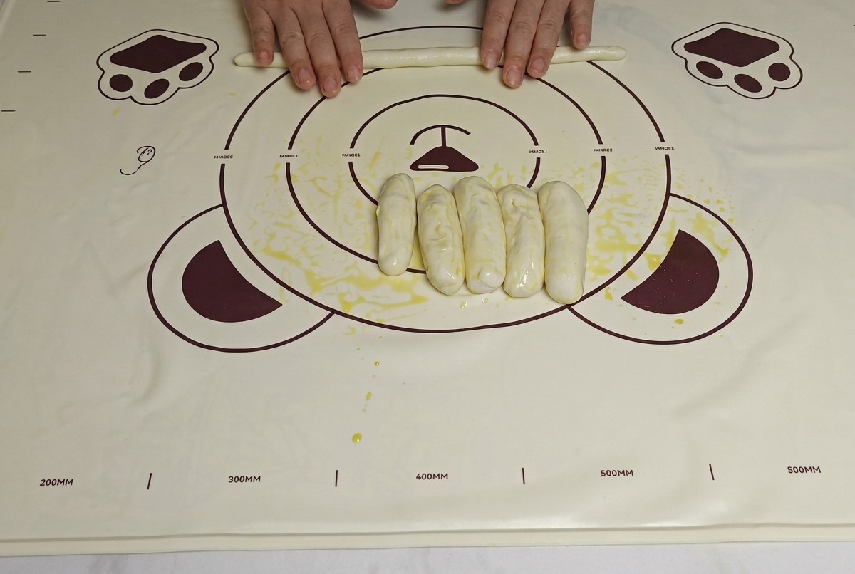 Mains roulant les bandes de pâte huilées sur un tapis, les rendant plus longues et plus fines.
