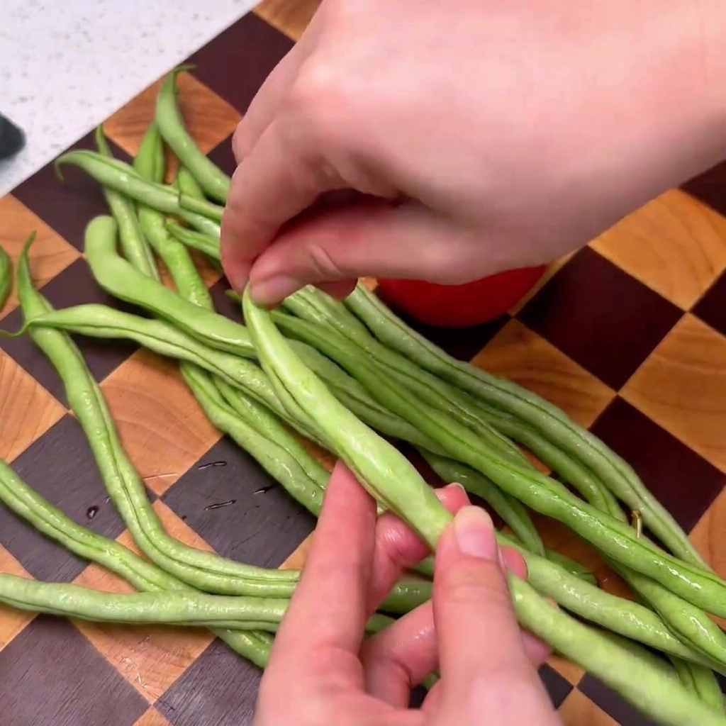 Haricots verts en train dêtre équeutés sur une planche à découper en bois.