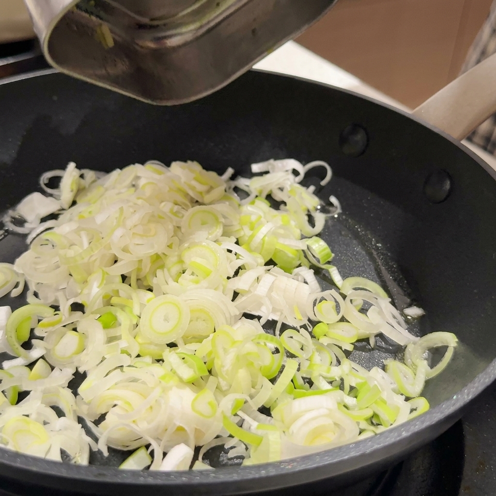 Oignons verts émincés et ail haché grésillant dans de lhuile de cuisson dans une poêle antiadhésive sombre.