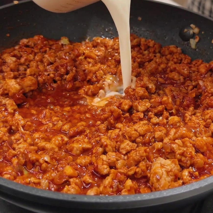 Lait de soja blanc et crémeux versé dun verre mesureur dans une poêle contenant la riche sauce au miso rouge.