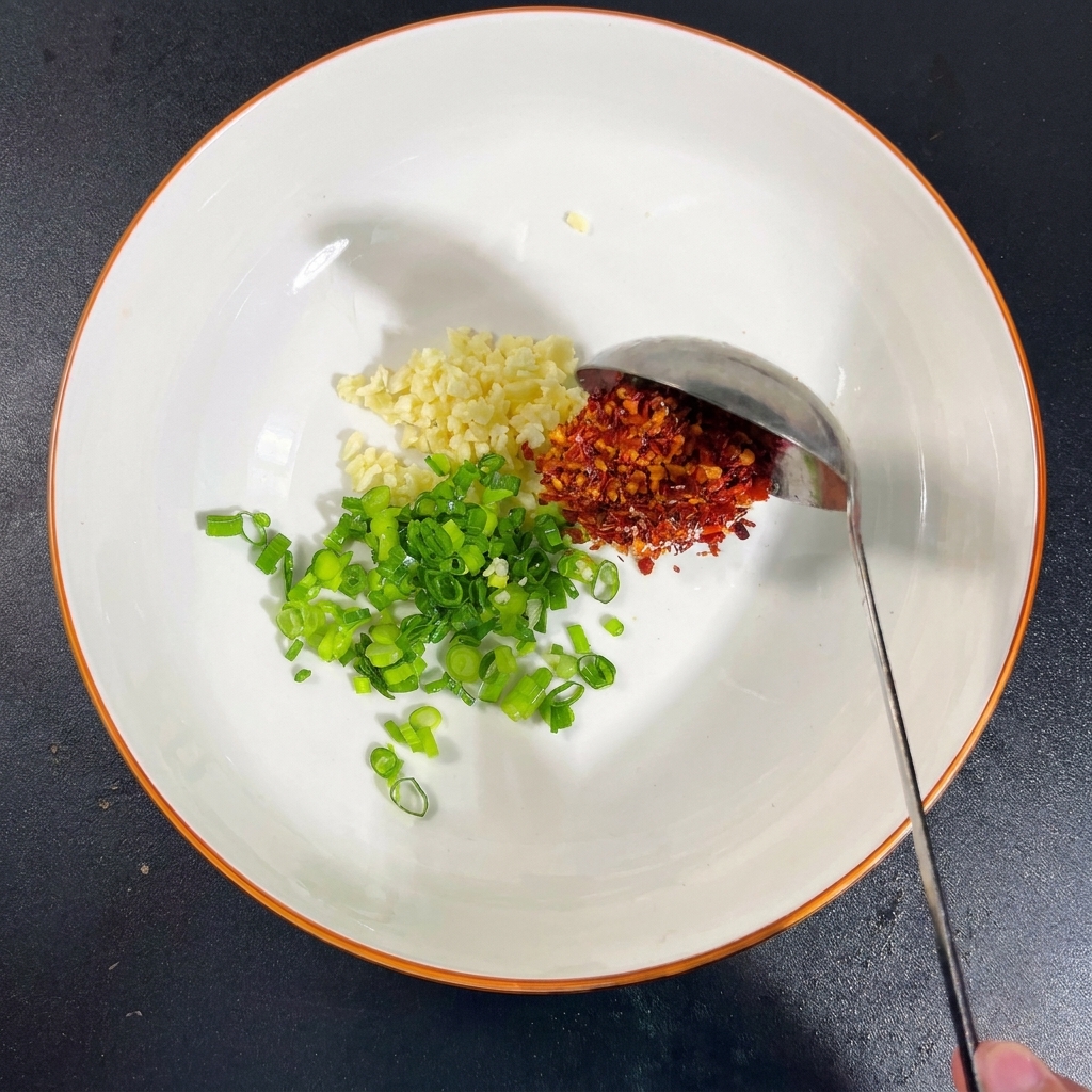 Un bol avec de lail, des ciboules, du sel, du MSG, des flocons de piment et un filet de sauce soja.