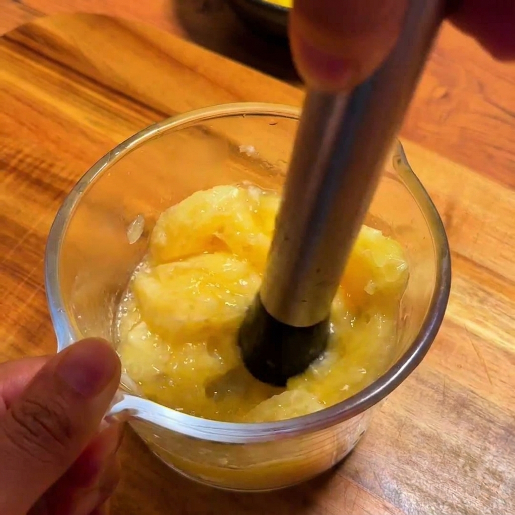 Un presse-agrumes en métal extrayant du jus de yuzu frais et vibrant dans une tasse à mesurer en verre.