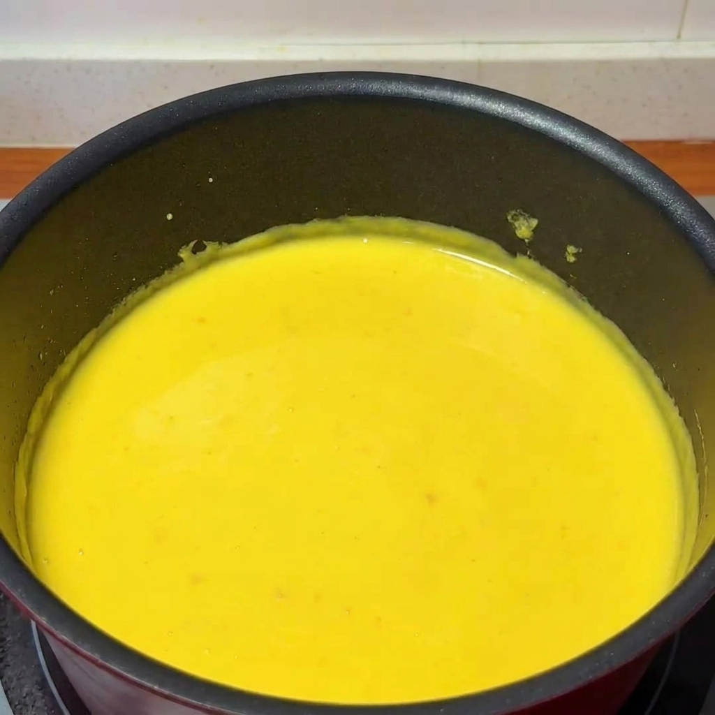 Une louche versant du jus de yuzu frais dans une casserole remplie de sauce au fromage épaisse et crémeuse, remuée par une cuillère en bois.