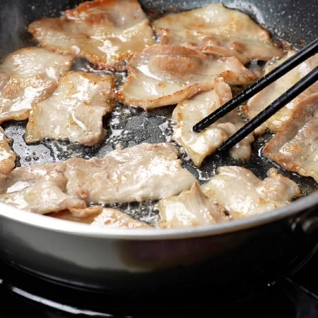 Tranches de poitrine de porc retournées dans une poêle révélant une coloration dorée.