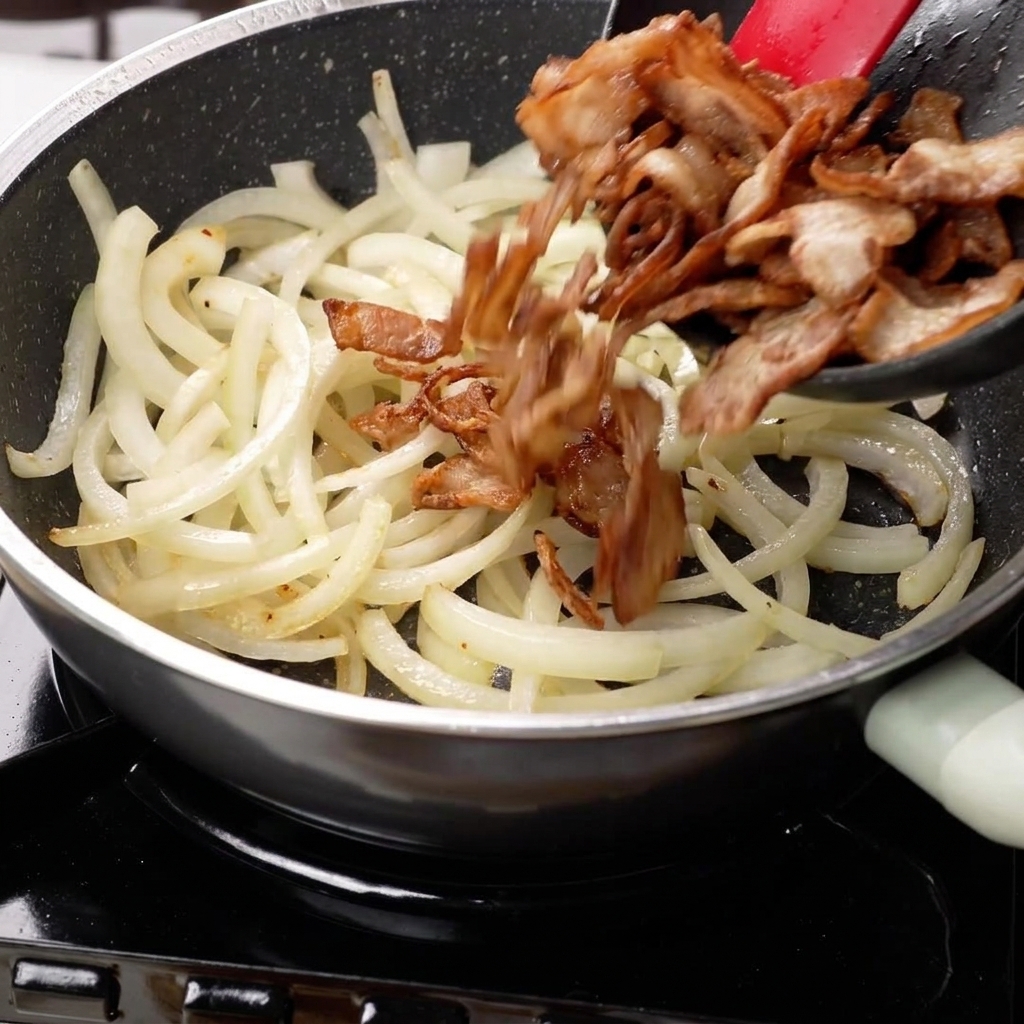 Oignons sautés et poitrine de porc saisie mélangés ensemble dans une poêle.