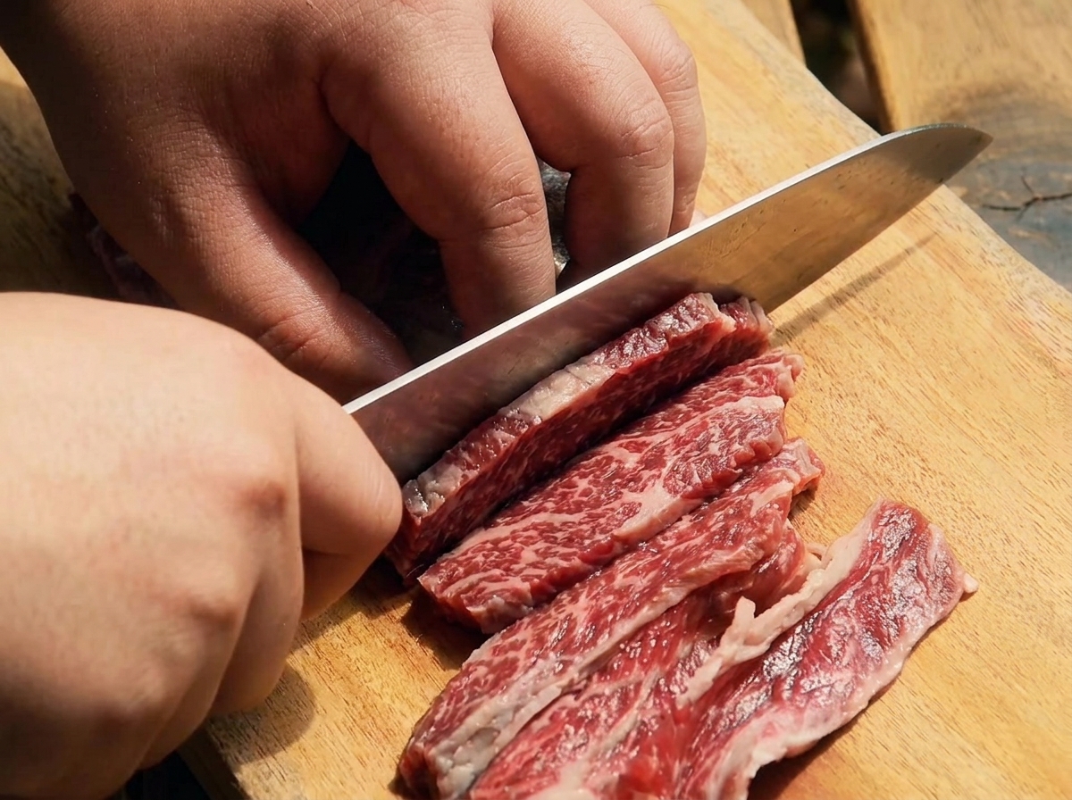 Un couteau bien aiguisé tranchant du bœuf en fines lamelles sur une planche en bois.
