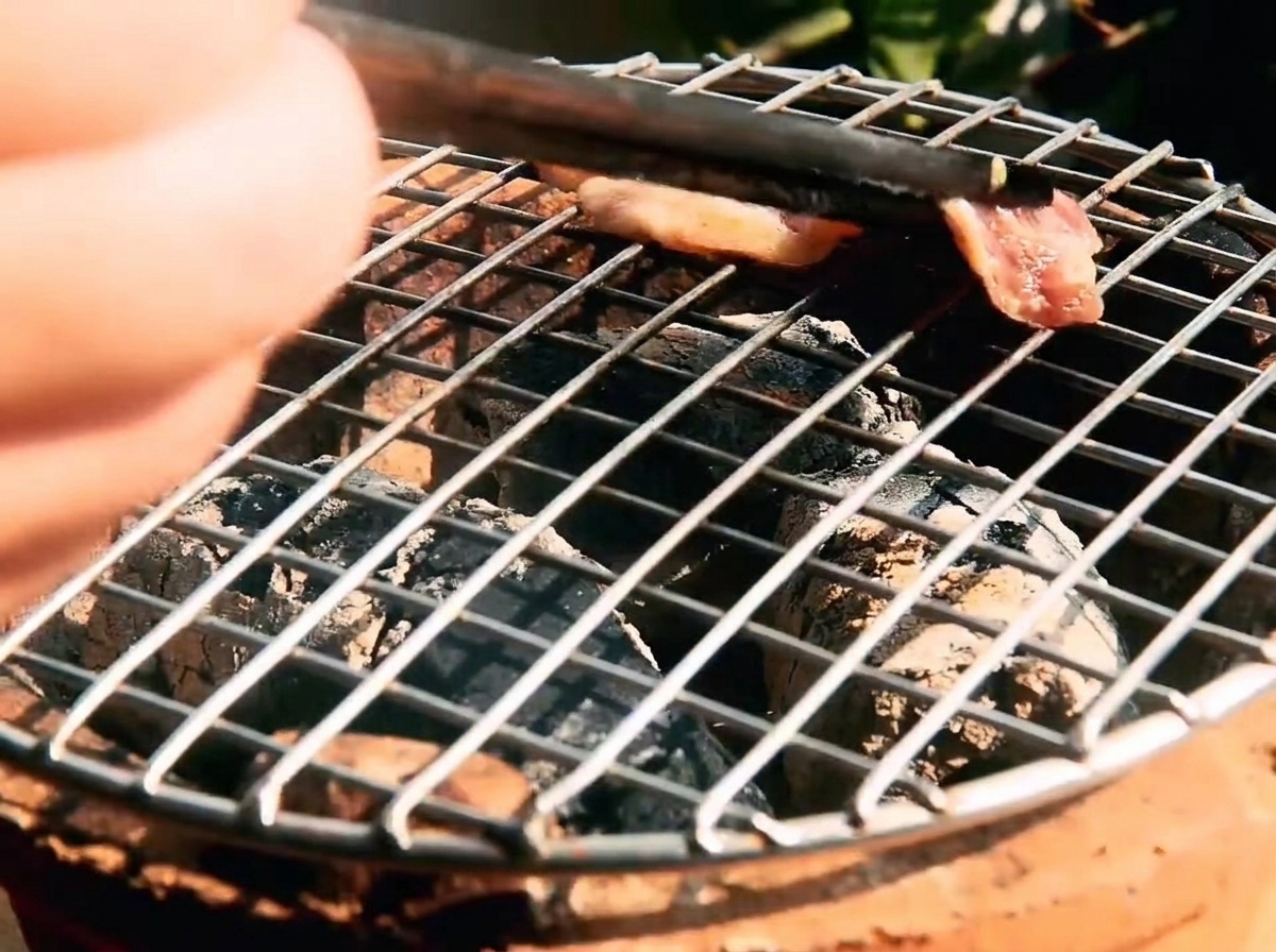 Tranches de bœuf marinées cuisant sur une grille chaude au-dessus de braises.