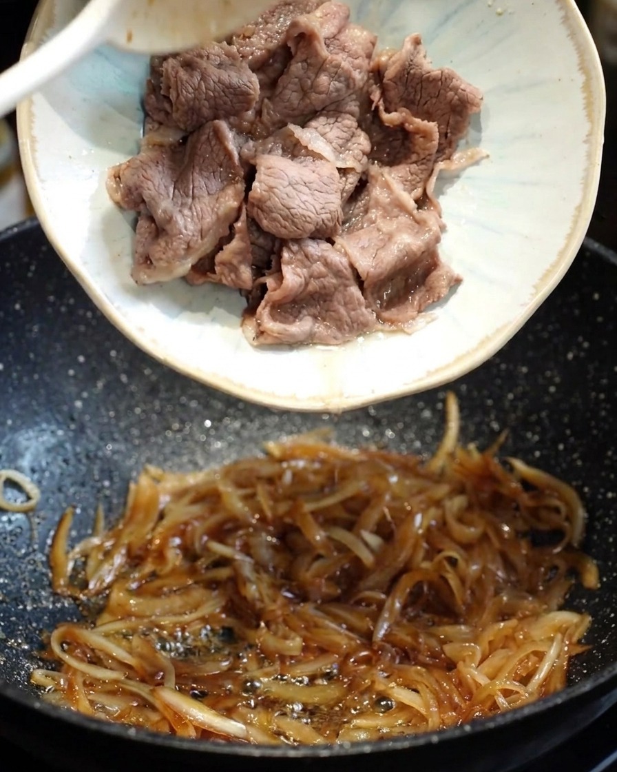 Une sauce teriyaki sombre et savoureuse versée dans une poêle avec les oignons et le bœuf.