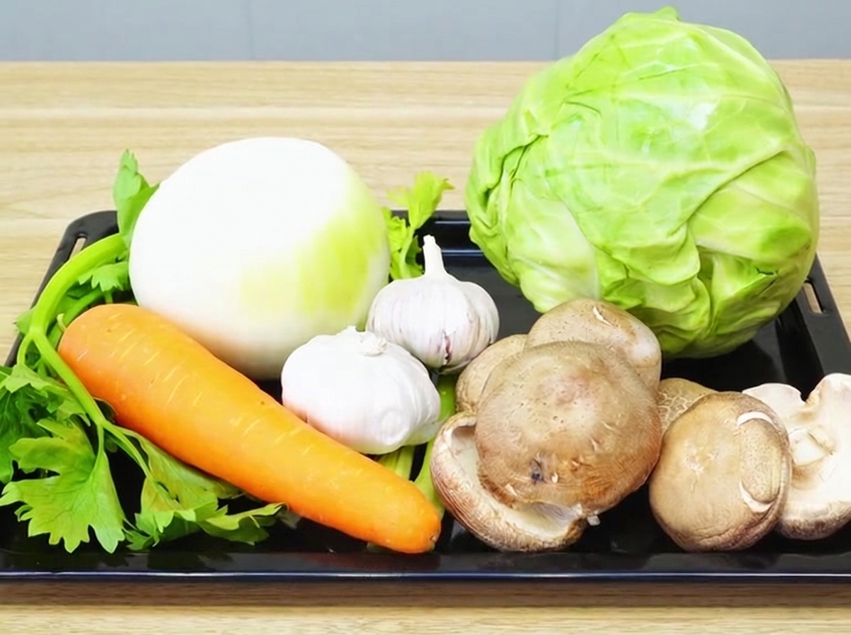 Une variété de légumes frais, dont oignon, ail, carotte, céleri, shiitake et chou, disposés sur une planche à découper en bois.