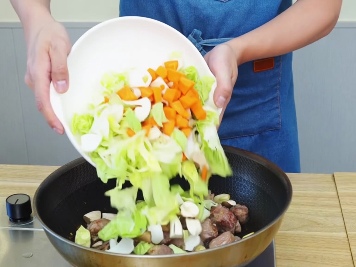 Légumes hachés et morceaux de bœuf mélangés et sautés ensemble dans une grande poêle.