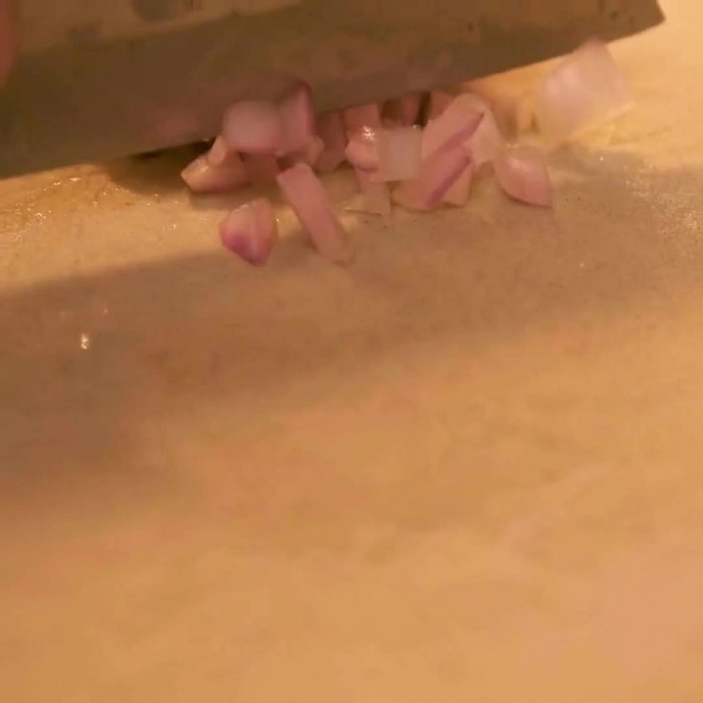 Vue rapprochée dun couteau aiguisé hachant finement un oignon rouge sur une planche à découper propre.