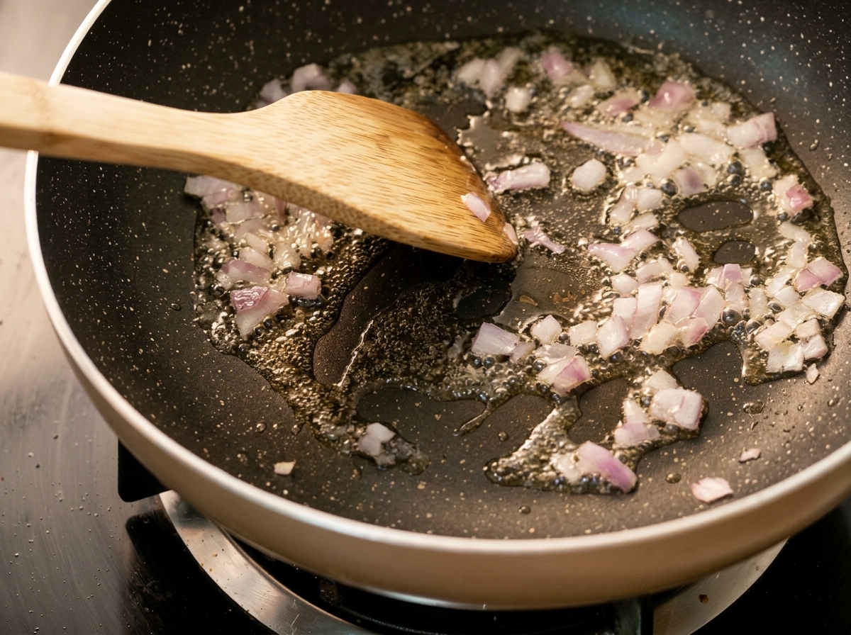 Oignons hachés cuisant dans une poêle chaude avec de lhuile, remués par une spatule en bois.