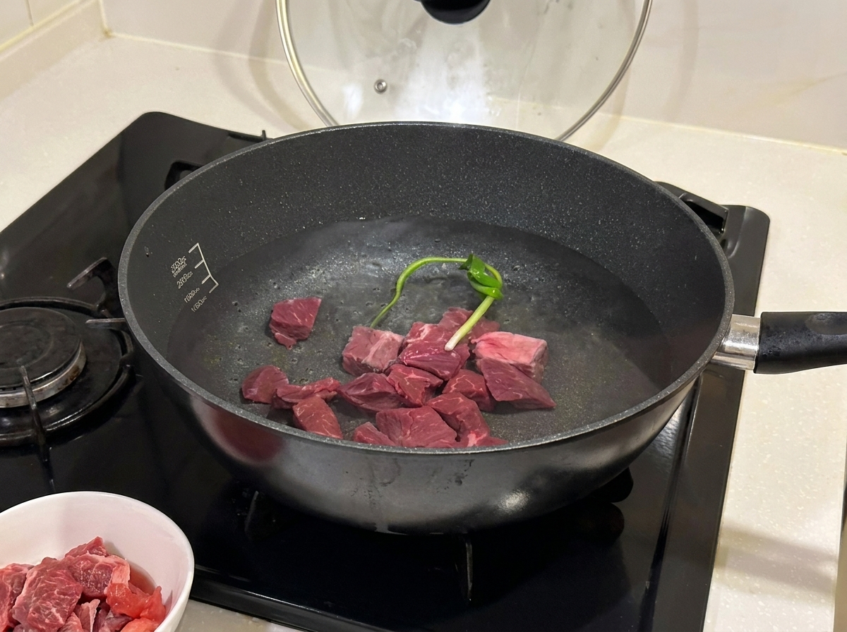 Morceaux de bœuf mijotant dans une casserole avec des aromates et du vin de cuisine.