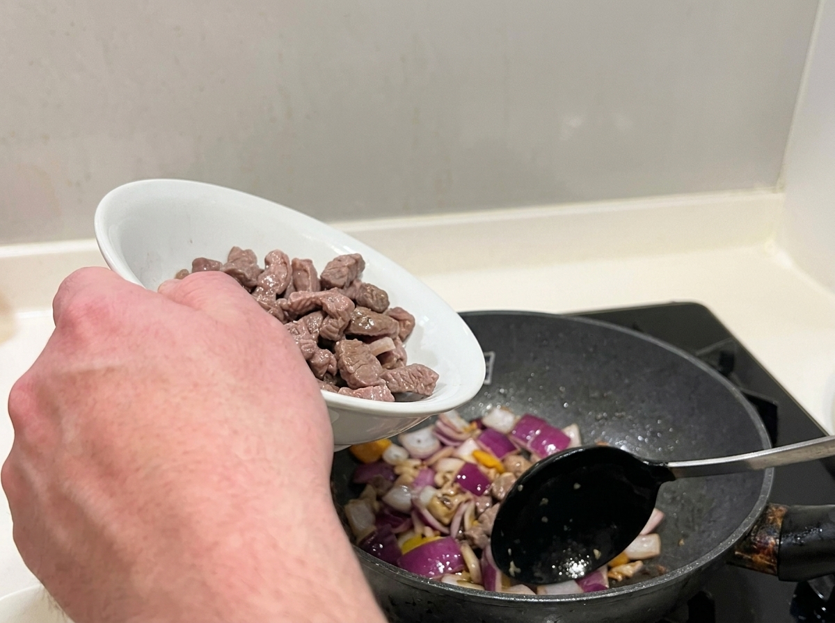 Morceaux de bœuf blanchis mélangés aux oignons rouges sautés dans une poêle.