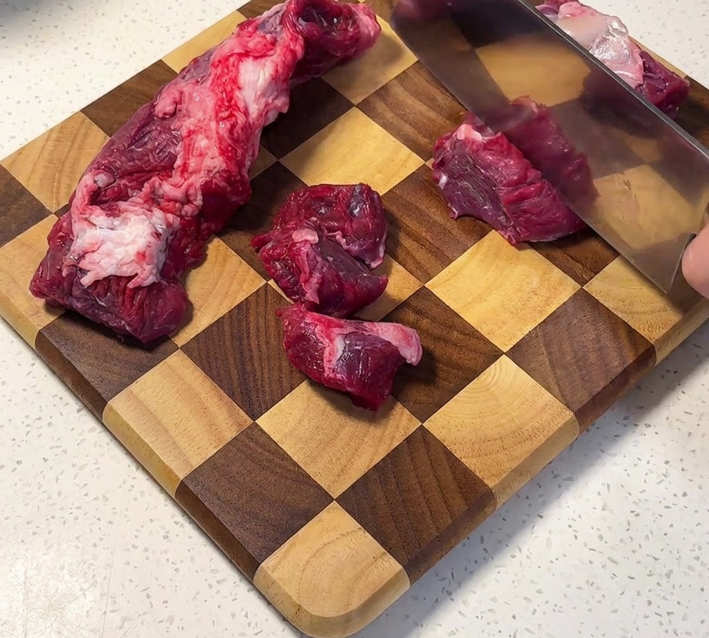 Poitrine de bœuf coupée en cubes uniformes sur une planche en bois.