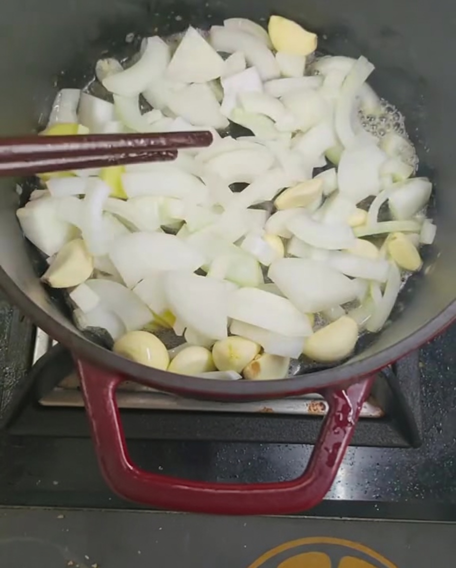 Oignons et ail sautant dans une marmite avec des baguettes.