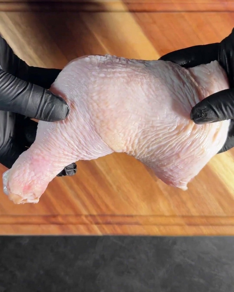 Une cuisse de poulet désossée posée à plat sur une planche à découper en bois.