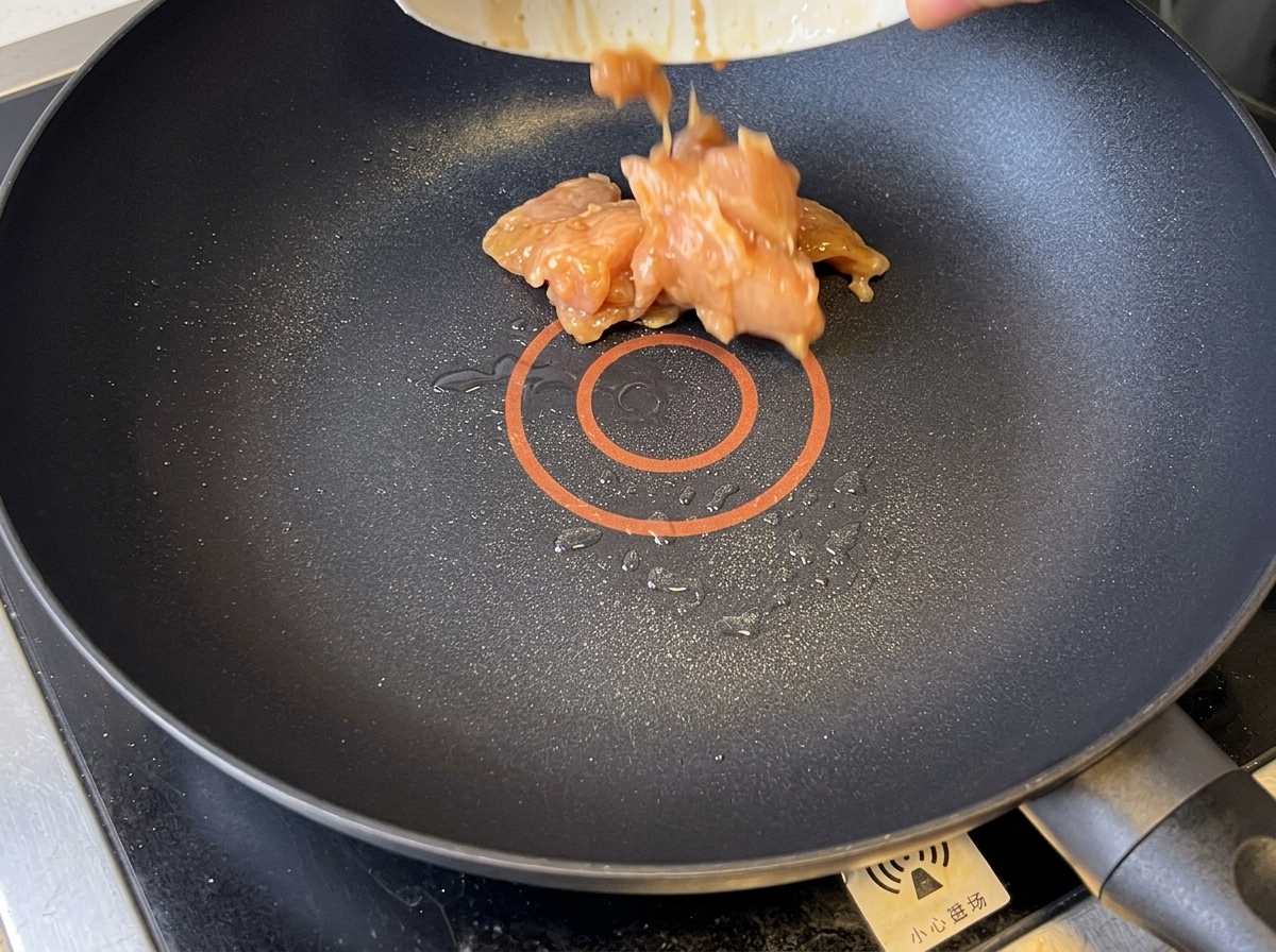 Morceaux de poulet dorés en cours de cuisson dans une poêle antiadhésive.