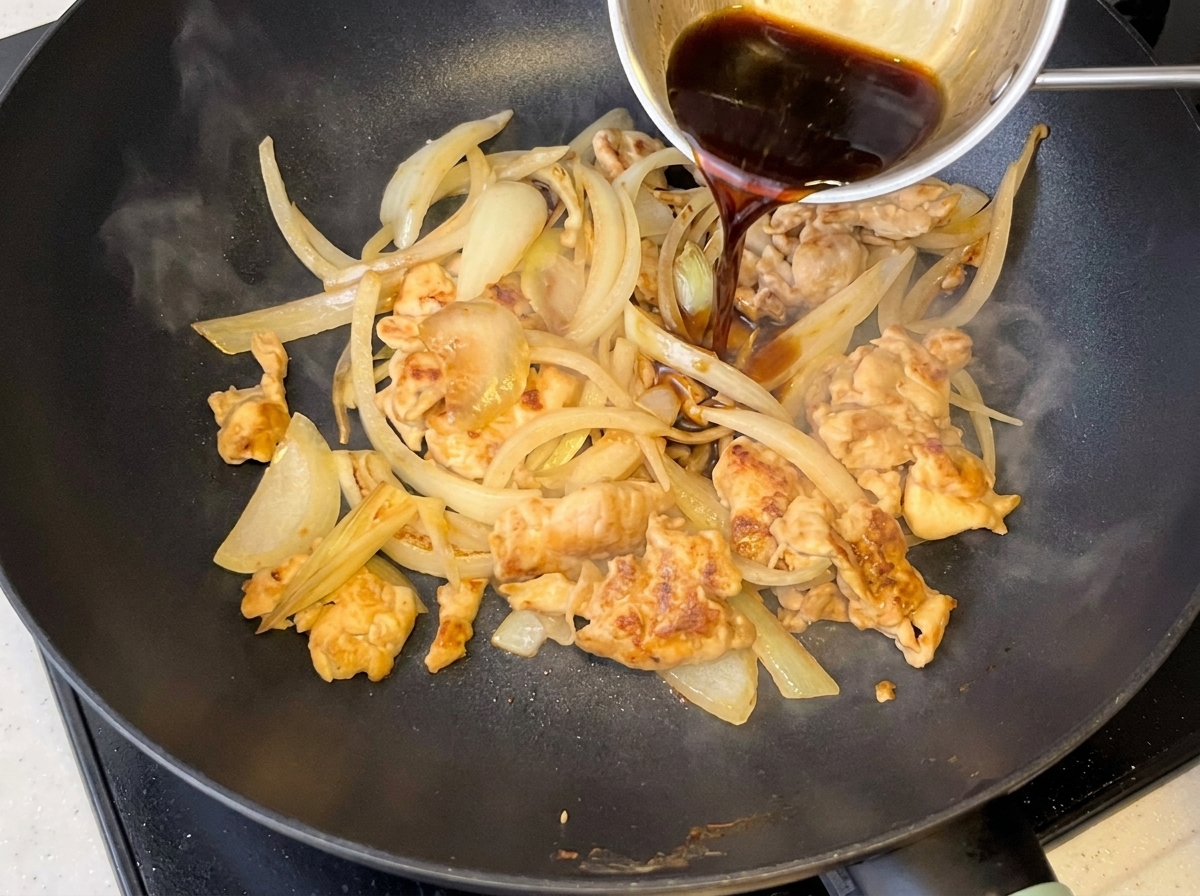 Sauce sombre versée dans une poêle contenant le poulet et les oignons.
