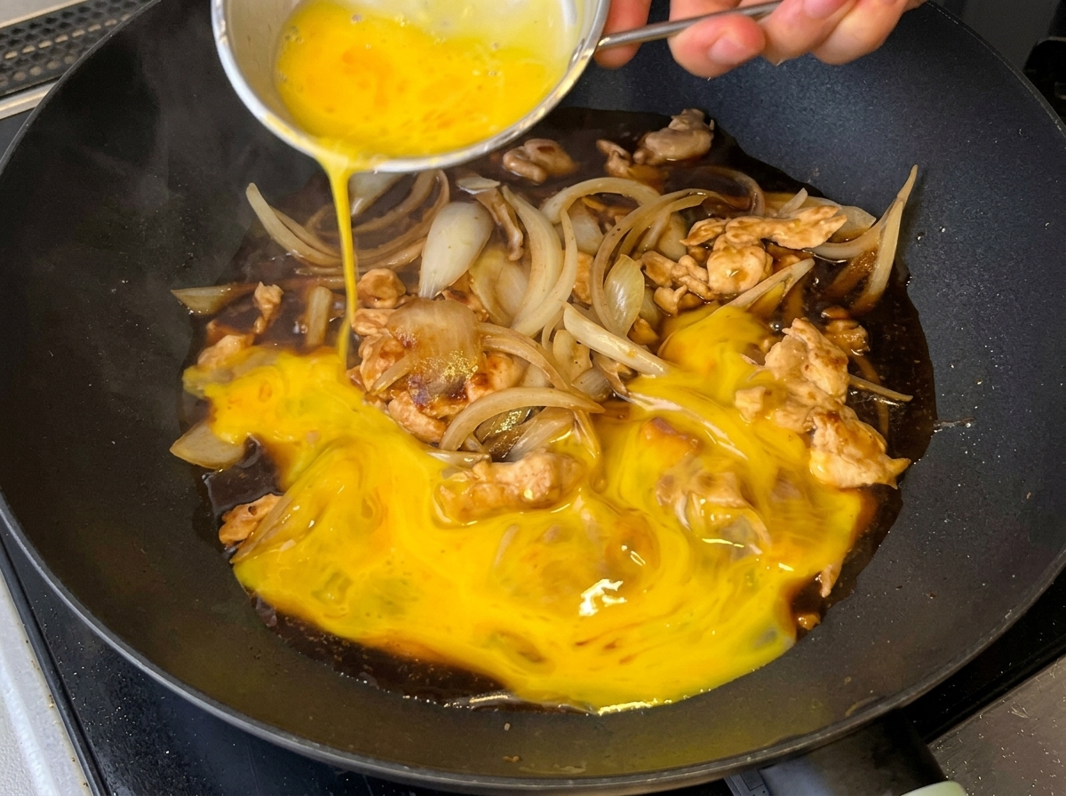 Œufs battus versés sur le mélange de poulet, doignons et de sauce.
