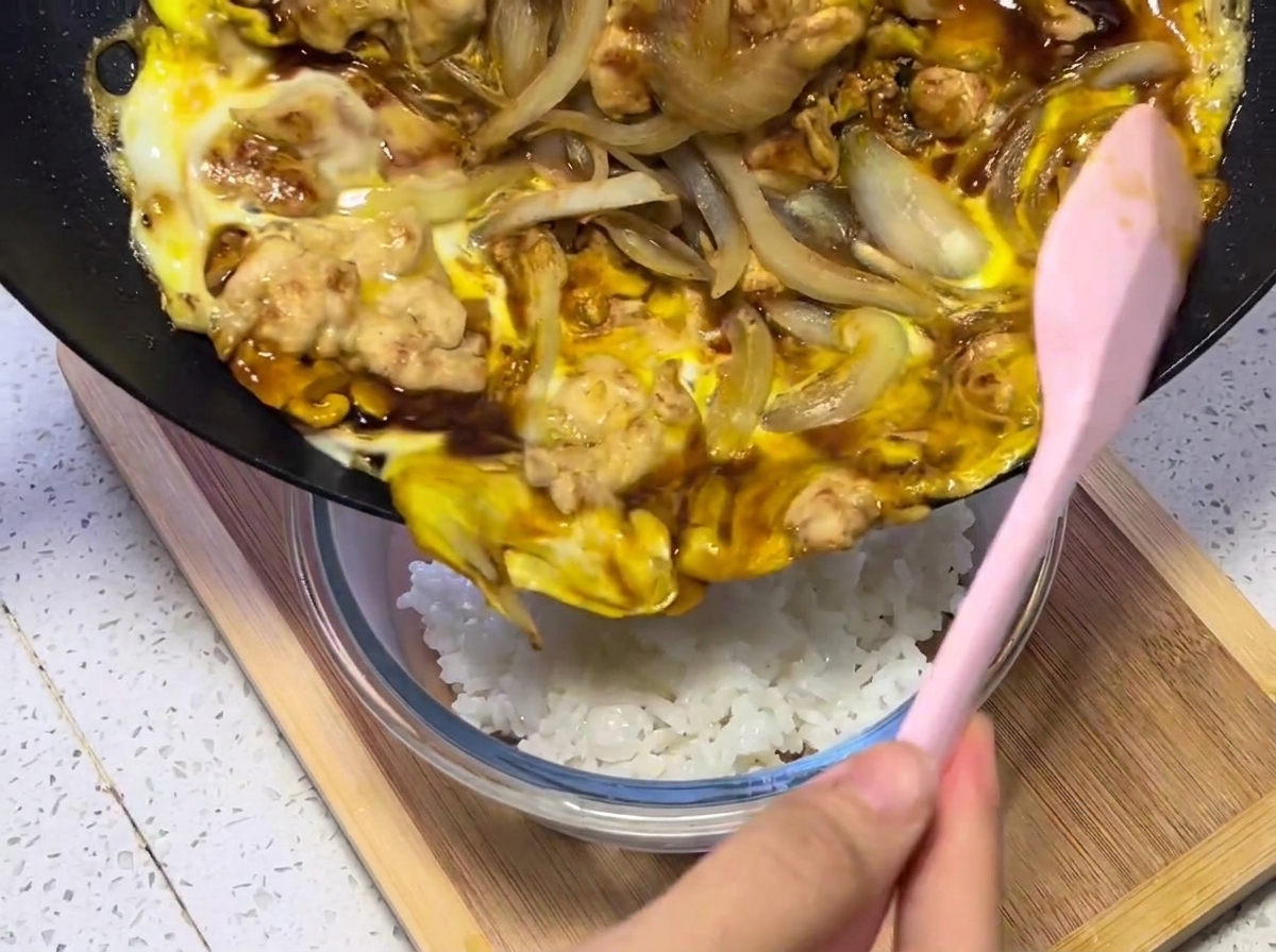Gros plan du mélange de poulet, œufs et oignons versé sur un bol de riz blanc fumant.