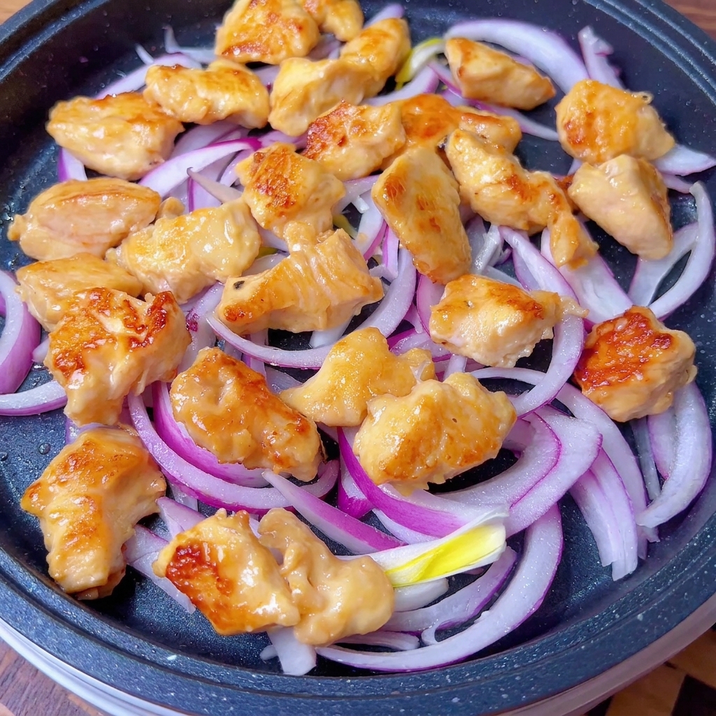 Poulet doré et oignons enrobés de sauce savoureuse dans une poêle.