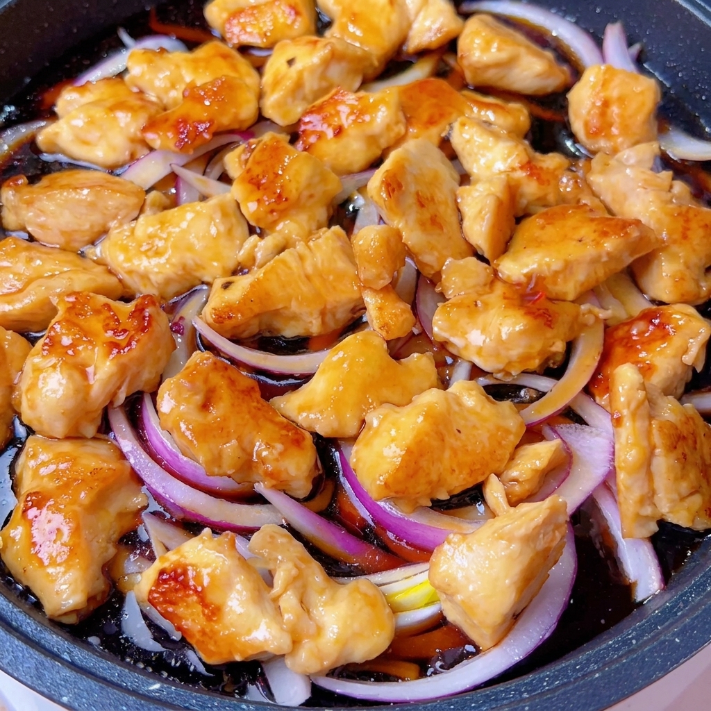 Une poêle couverte sur le feu avec le mélange de poulet et doignons qui mijote.