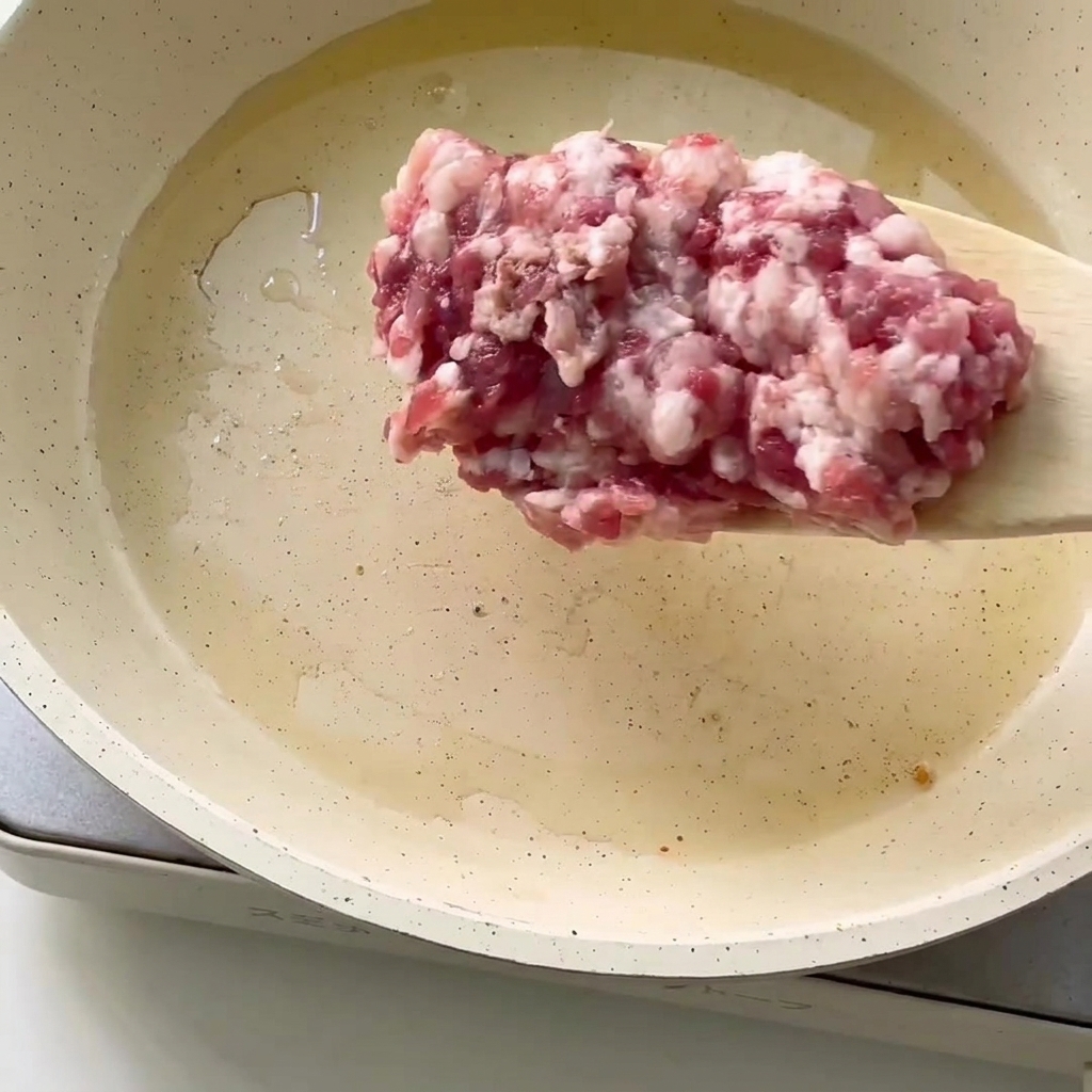 Gros plan sur de la viande hachée ajoutée dans une poêle avec de lhuile chaude.