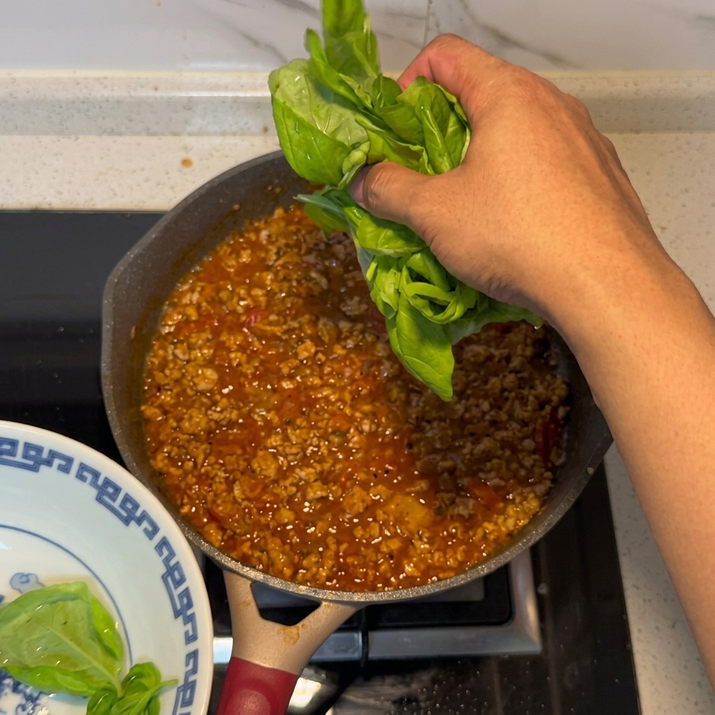 Feuilles de basilic frais ajoutées à la sauce à la viande et à la tomate terminée.