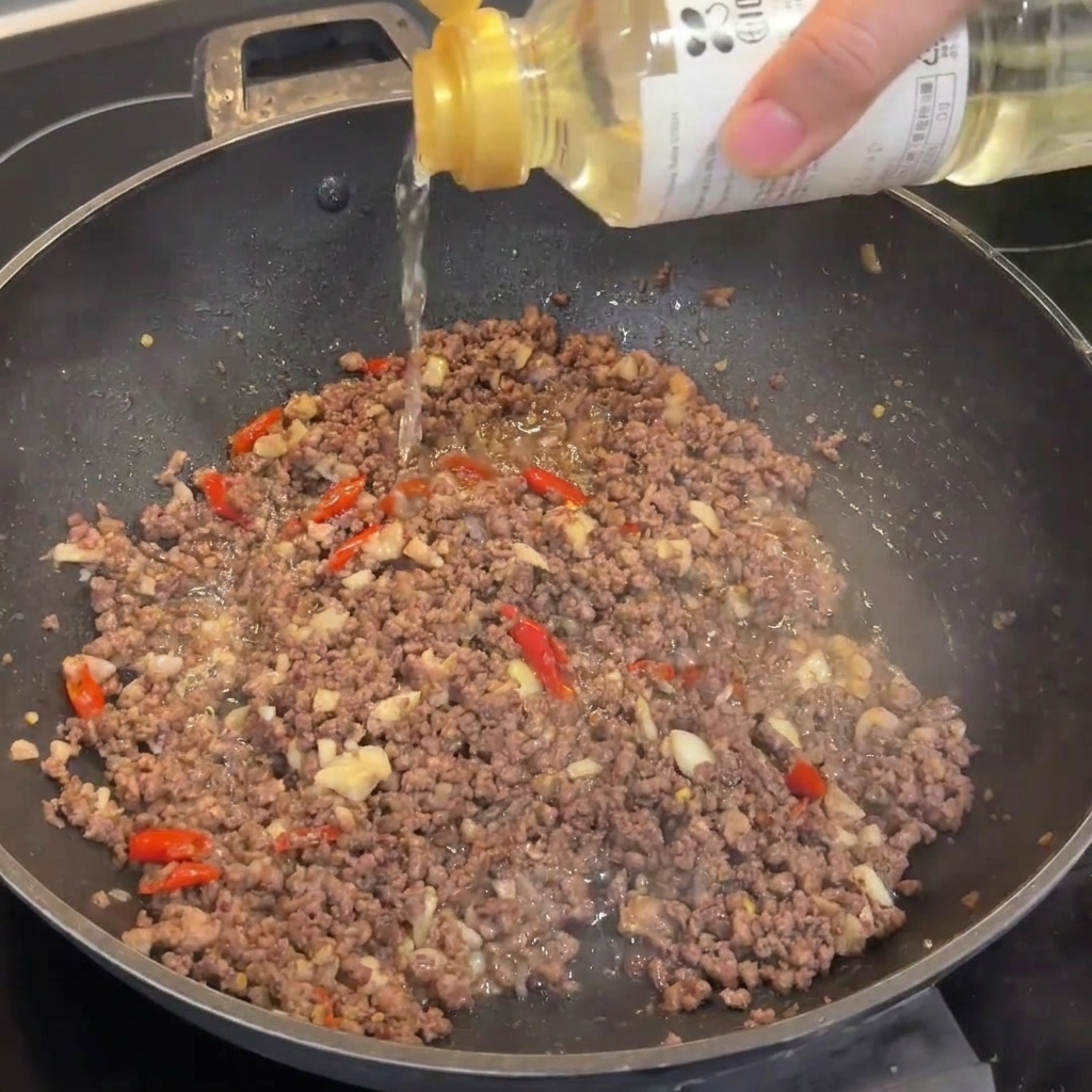 Un filet de vin de riz versé dans le wok contenant le bœuf bruni.