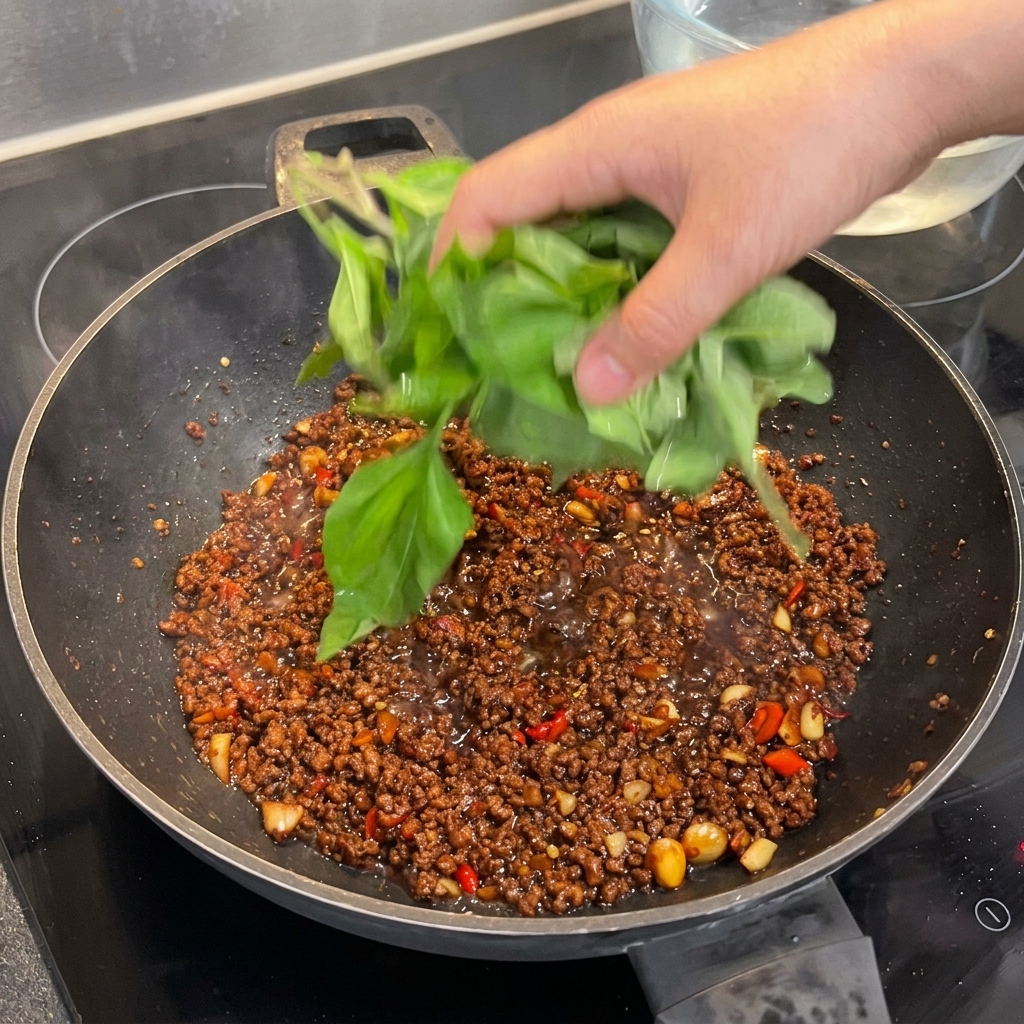 Une grosse poignée de feuilles de basilic sacré frais ajoutée au wok, prête à flétrir.