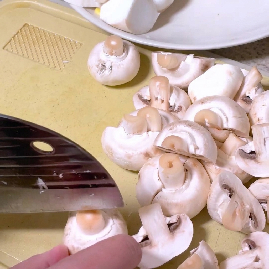 Champignons de Paris coupés en deux sur une planche avec un couteau de cuisine.