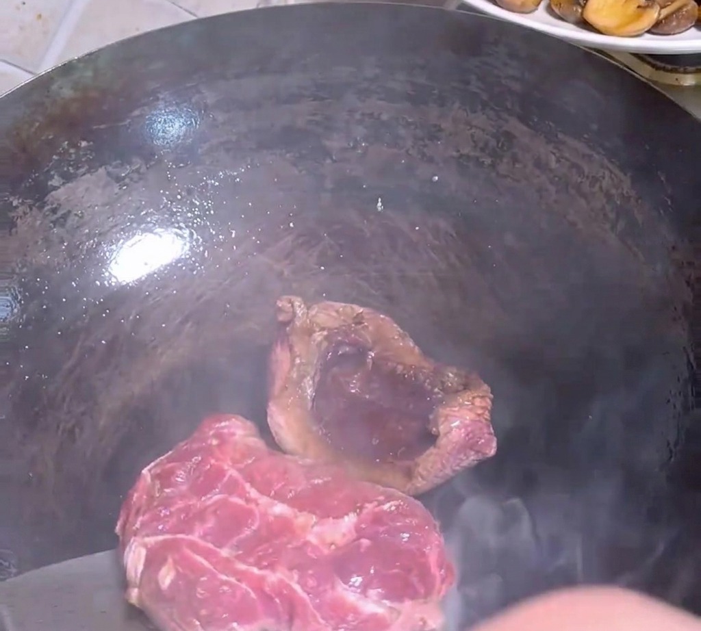 Spatule en métal retournant un morceau de bœuf partiellement saisi dans un wok sombre.