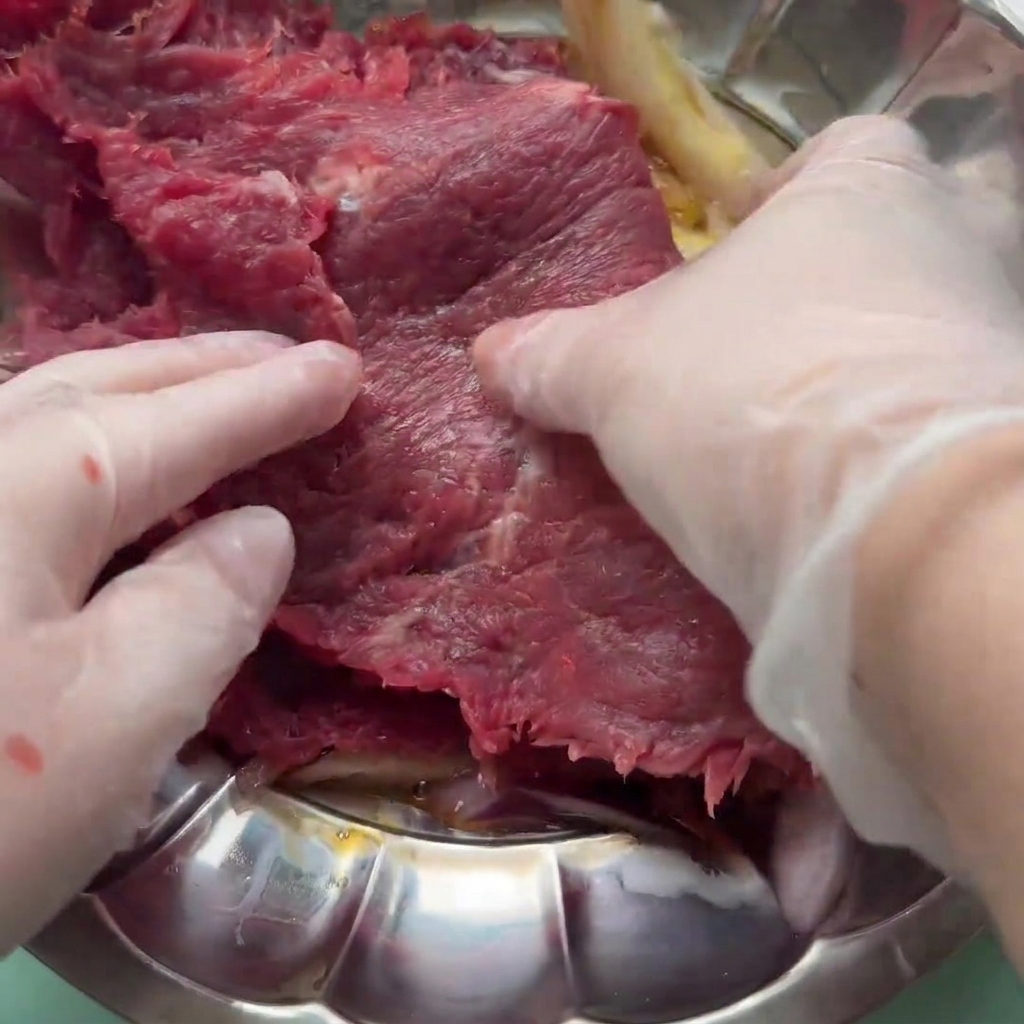 Une tranche de bœuf cru mélangée dans une marinade à base dœuf, doignon et de sauces dans un bol.