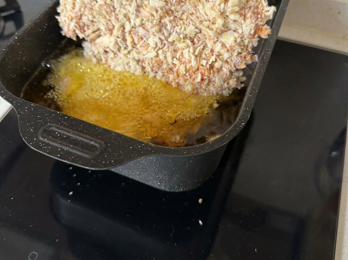 Une côtelette de bœuf panée en train de frire dans une poêle remplie dhuile chaude bouillonnante.